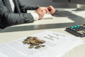 Cropped view of businessman writing in notebook near coins and petitions for bankruptcy on table, on